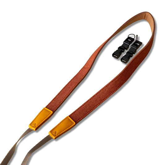 Brown camera strap with yellow buckle and black clips on a white background